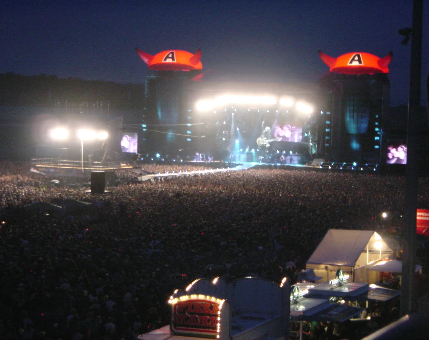 Open-air rock concert at night with a crowd of tens of thousands in front of the stage